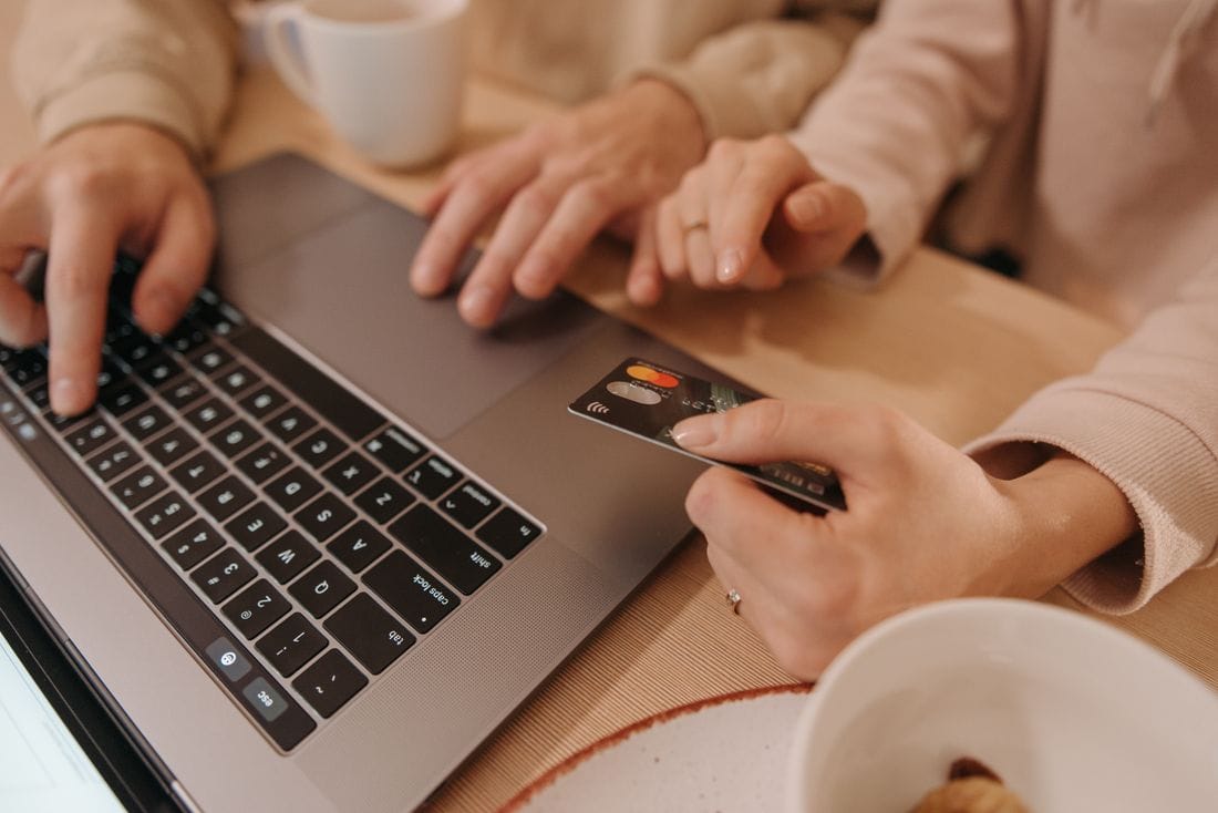 Cartões bancários sobre notebook e pessoa realizando compras online